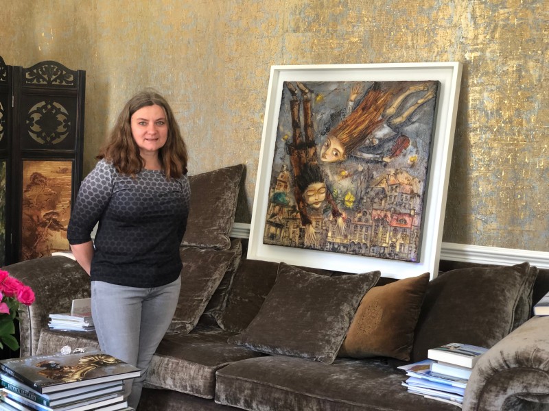 Irish Artist Ludmila Korol with her original oil painting 'Living the Dream' hanging painting on gold coloured handmade wallpaper
