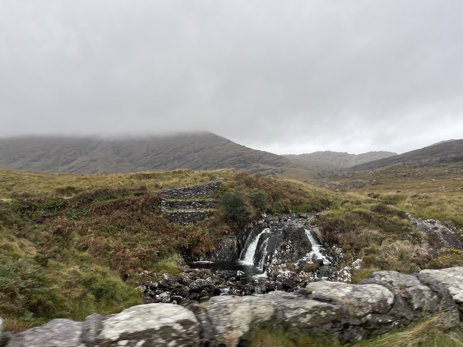 Water spilling over dark rock beneath low cloud.